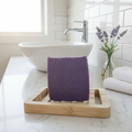 Purple soap on a wooden soap dish with a bathroom setting in the background
